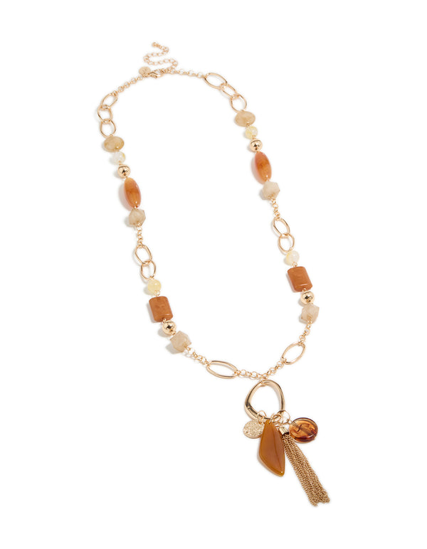 Explore this long beaded necklace with balls, beads, charm elements, and tassel fringe in gold statement styling front view