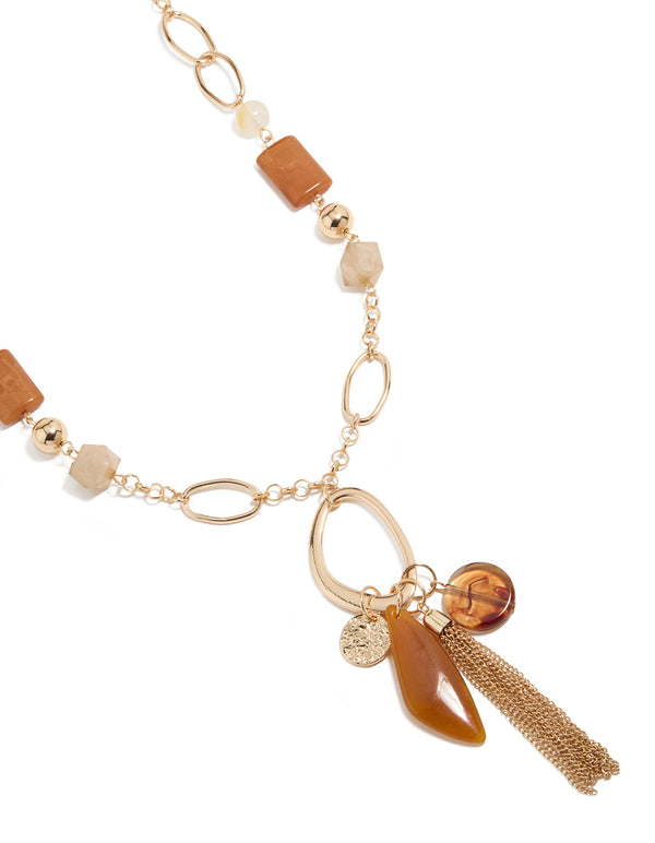 Showcasing a long beaded necklace featuring balls, beads, charm details, and tassel fringe in gold with statement styling close up view