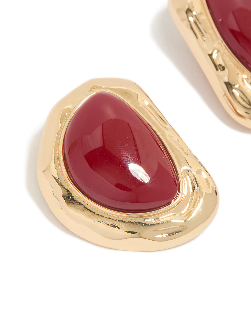 Featuring statement stud earrings with organic textured design and dark red stone in gold finish close up view