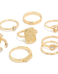 Highlighting Roman numeral engravings and textured metalwork on dainty gold rings with clear diamante accents close up view - link has visual effect only
