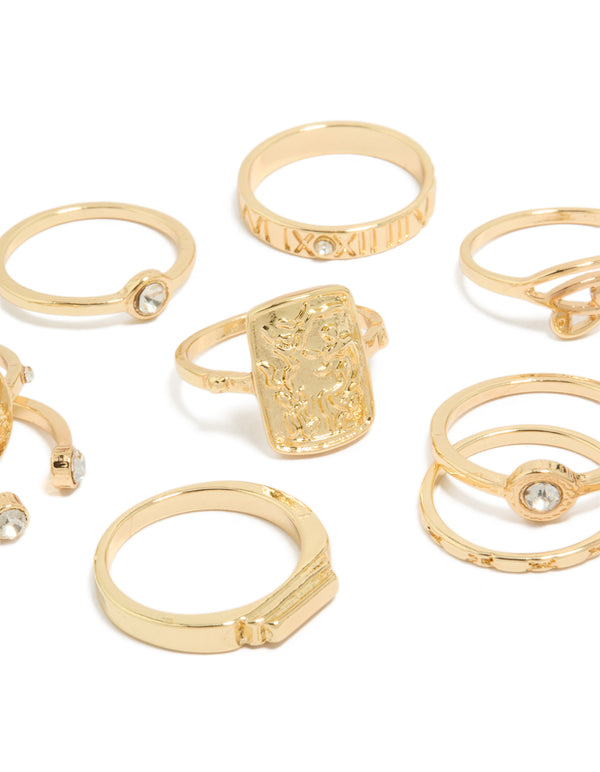 Highlighting Roman numeral engravings and textured metalwork on dainty gold rings with clear diamante accents close up view