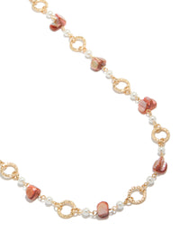 Showcasing a gold open circle long statement necklace with beads and pearls in pink coral and white tones close up view - link has visual effect only
