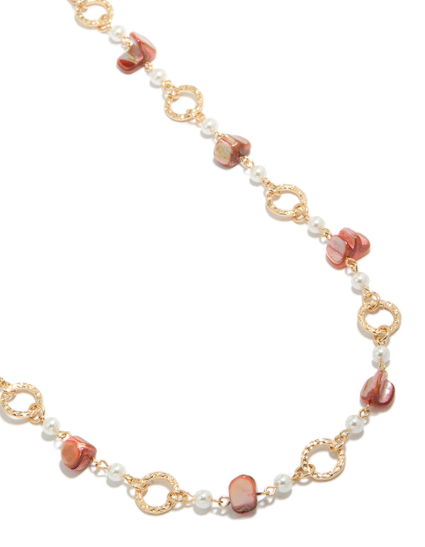 Showcasing a gold open circle long statement necklace with beads and pearls in pink coral and white tones close up view