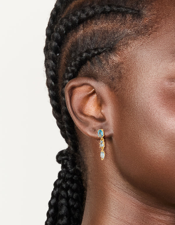 Featuring statement gold plated light blue cubic zirconia trip drop earrings in aqua on ear view
