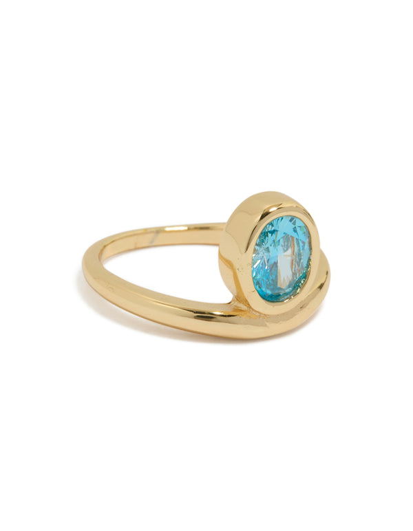 Showcasing a gold plated stainless steel statement ring with oval cut blue cubic zirconia crystal in aqua front view